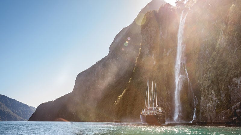 Milford sound ship sun shining over cliffs