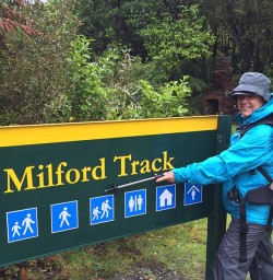 Happy hiker in rain by sign at end of Milford Track